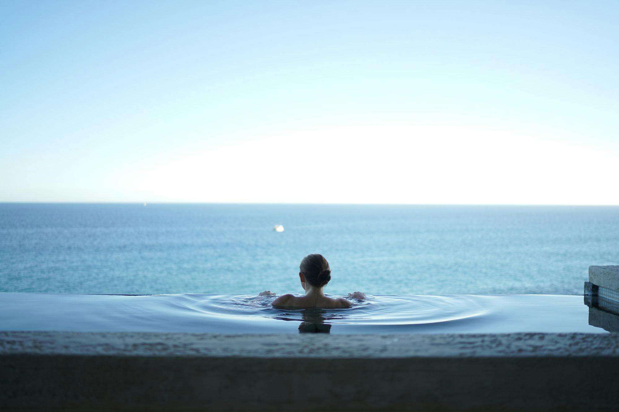 Woman at the edge of an infinity pool staring out at the ocean.